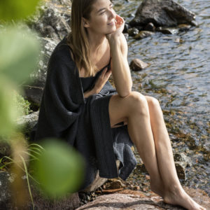 Woman sitting outside in the nature with rento sauna towel wrapped around her